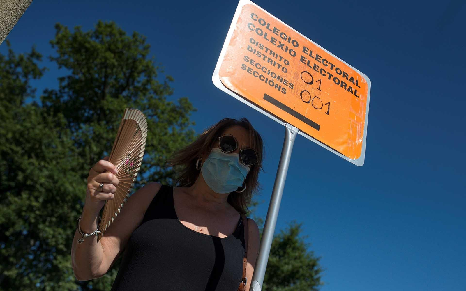 Una mujer combate el calor junto a una señal de colegio electoral en Pereiro de Aguiar donde el coordinador de prevención de las elecciones de la Xunta, Emilio de la Iglesia, ha mostrado las medidas de seguridad que se aplicarán. EFE/Brais Lorenzo