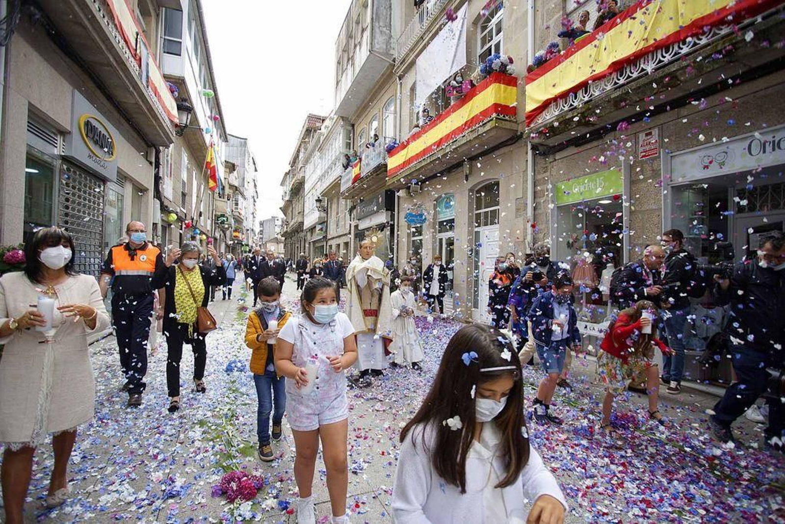 No hubo las tradicionales alfombras florales ni los fieles participaron en la siempre multitudinaria procesión, limitada al paso de la Custodia portada por el párroco mientras los fieles lanzaban pétalos desde los adornados balcones y con compañia de los niños de Primera Comunión con mascarillas
