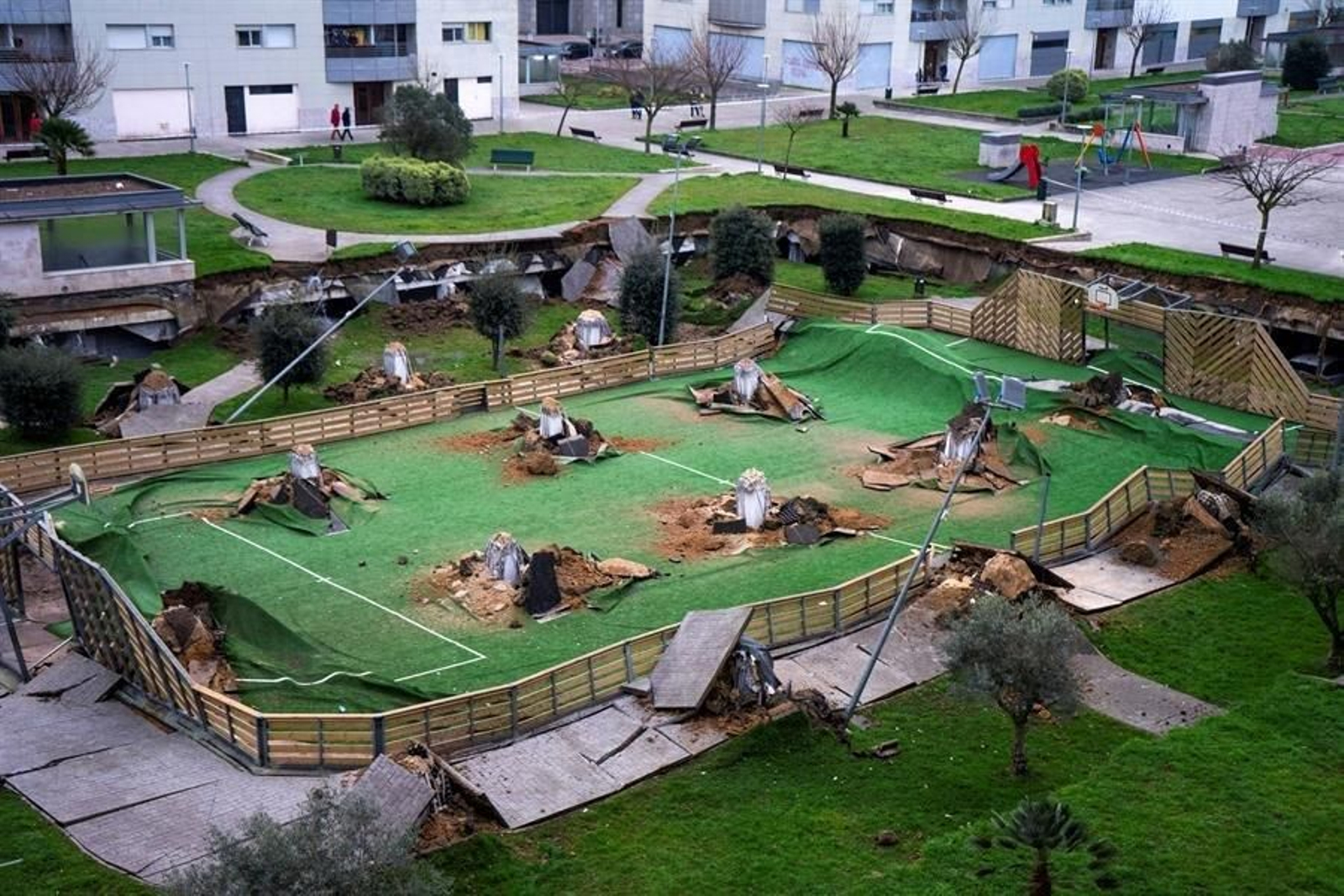 Vista del parque infantil y la pista deportiva que se ha hundido sobre un aparcamiento de una urbanización en el barrio de Nueva Montaña de Santander