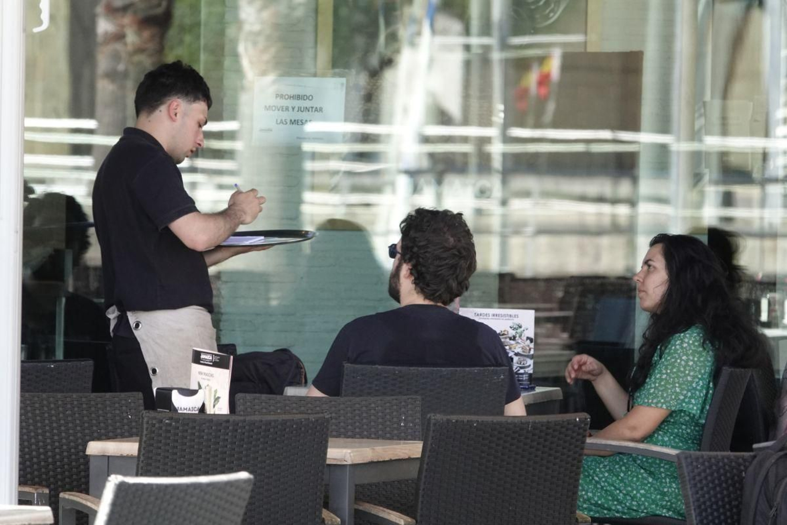 Un camarero atiende a dos clientes en una terraza.