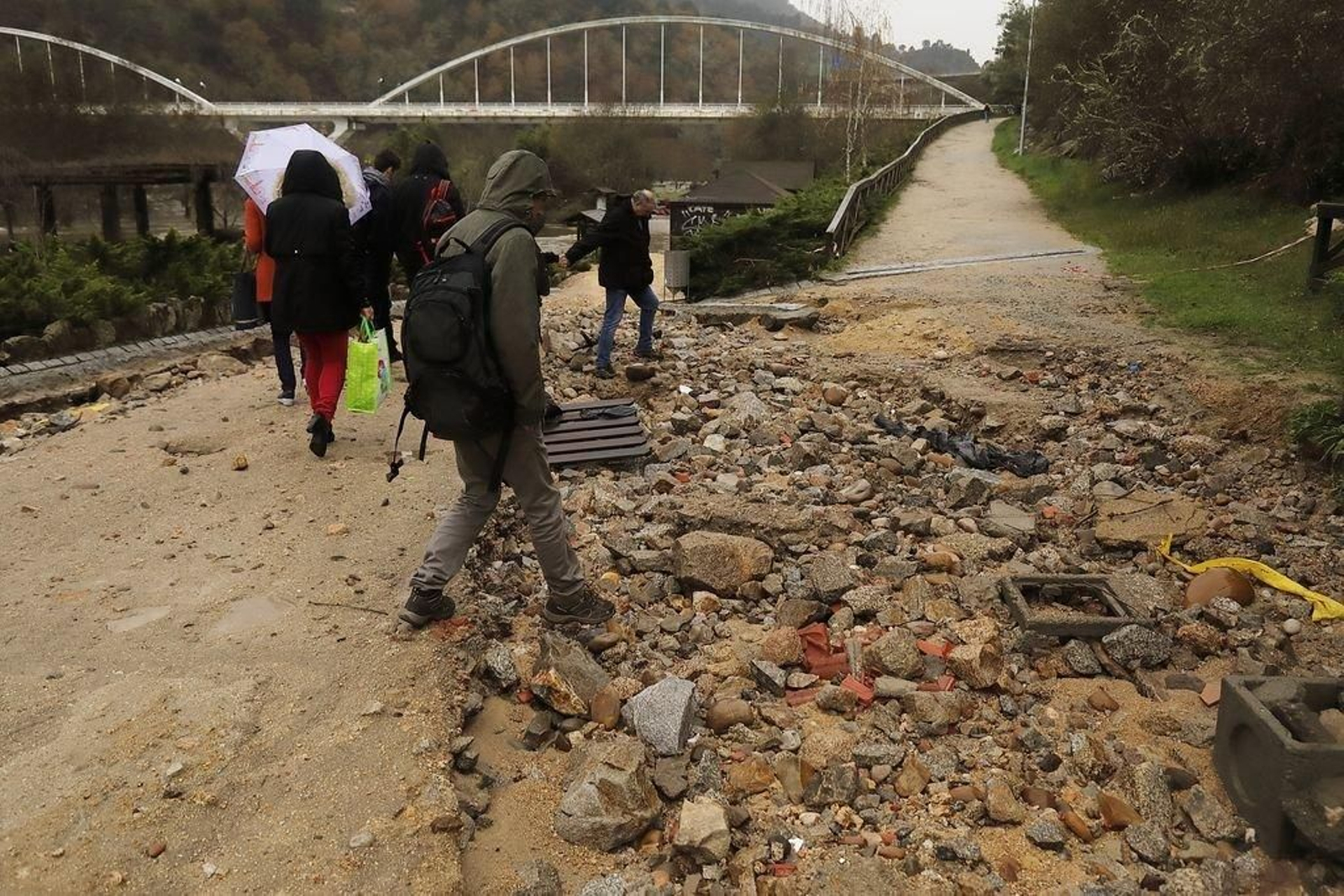 Bañistas cruzan por entre los socavones que ocasionó el río Miño en la pista de acceso a las termas públicas de Outariz.