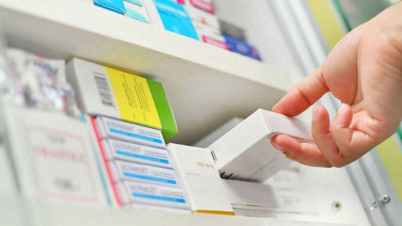 Una farmacéutica deposita un medicamento en una estantería de una farmacia.