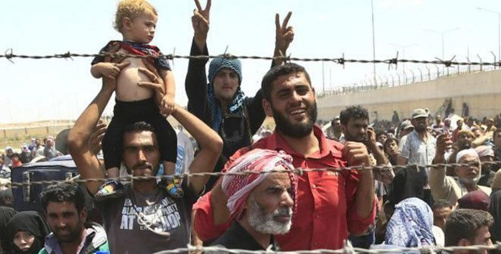 Un grupo de ciudadanos sirios ante la alambrada de un campo de refugiados