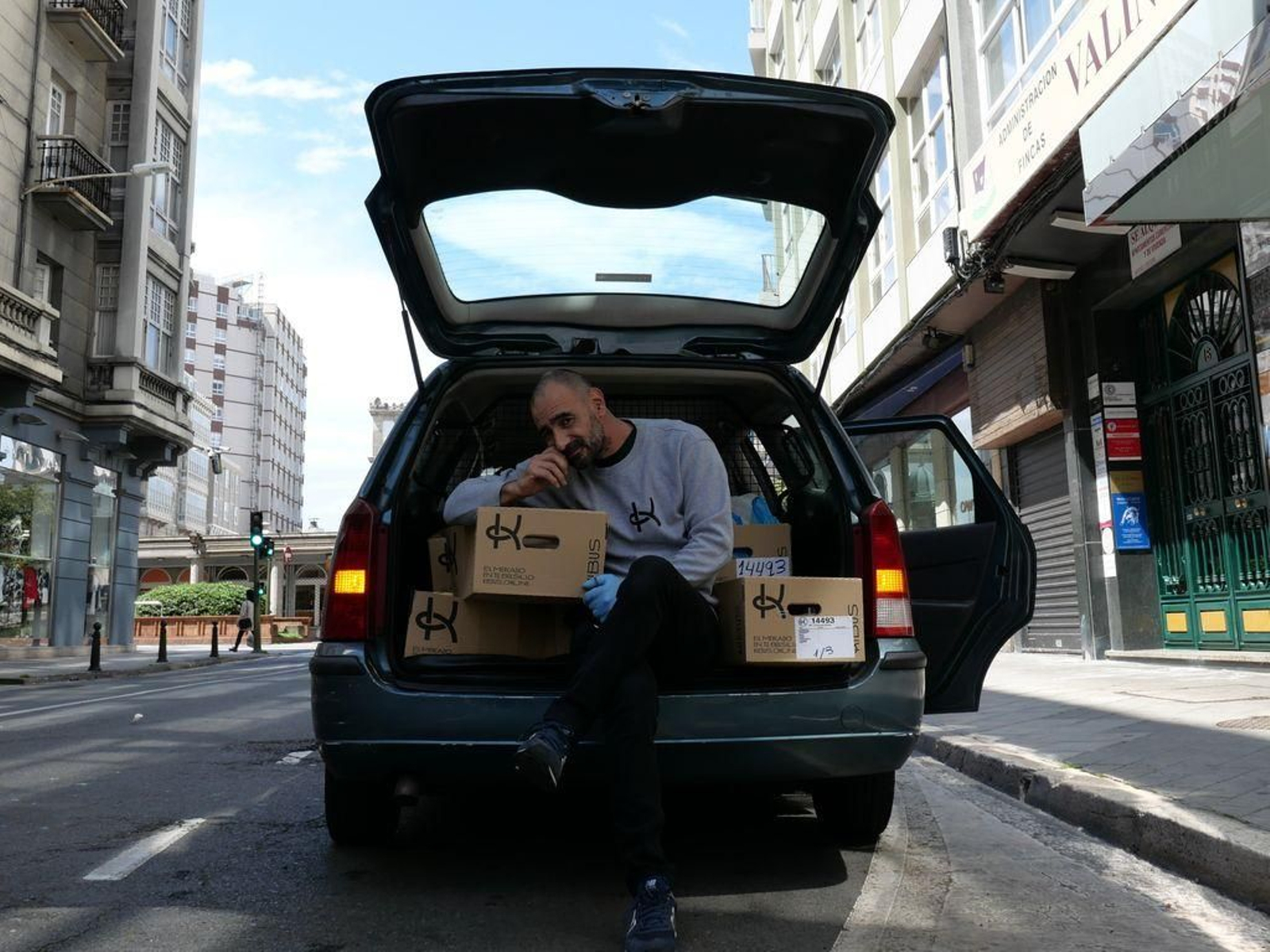 Pablo Rivas sujeta una caja de reparto como una tabla de surf y un surfista en A Coruña.