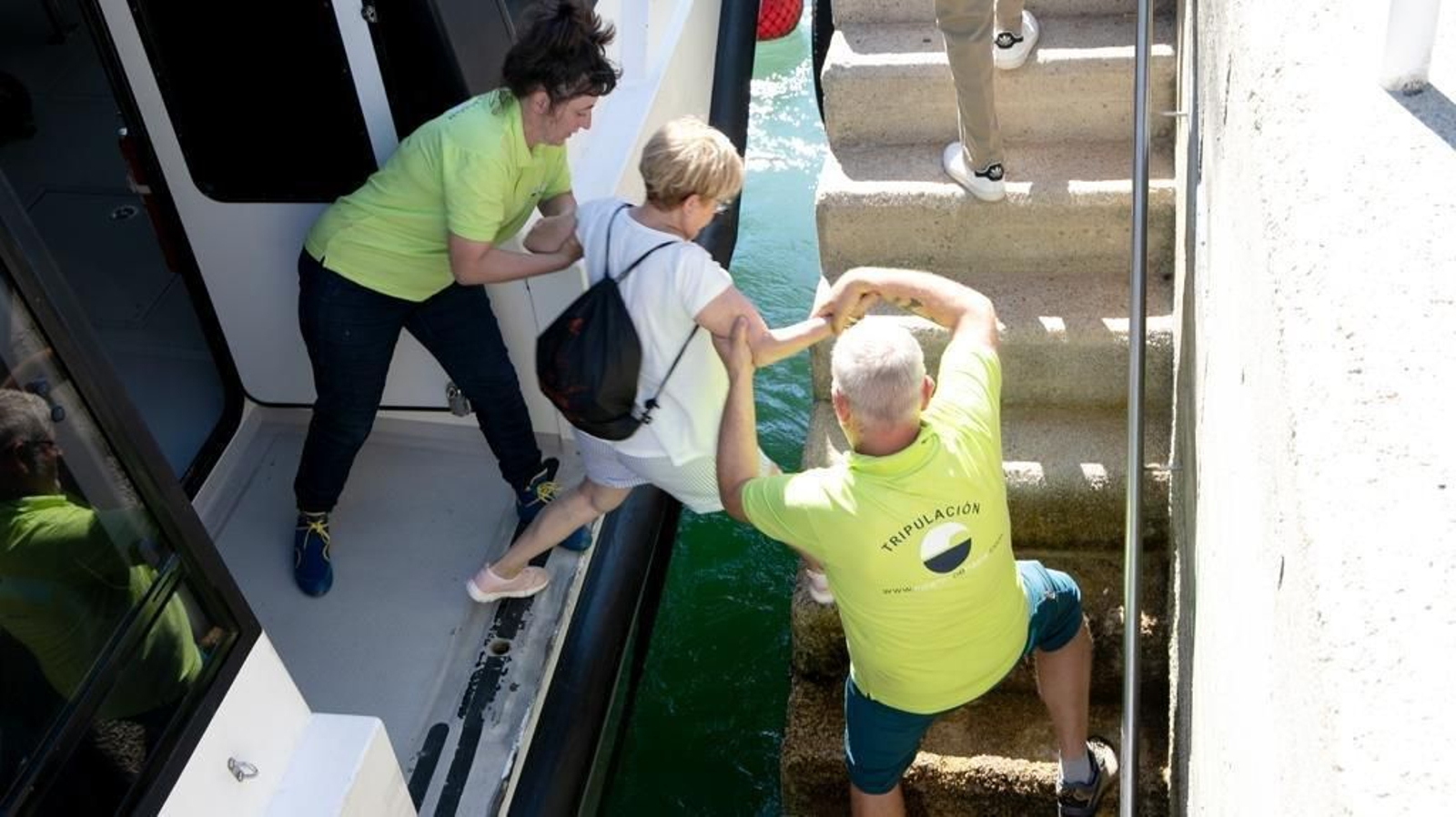 Dos tripulantes de Nabia, esta misma mañana, ayudan a una pasajera a saltar desde el muelle de piedra de Cangas al barco de Nabia.