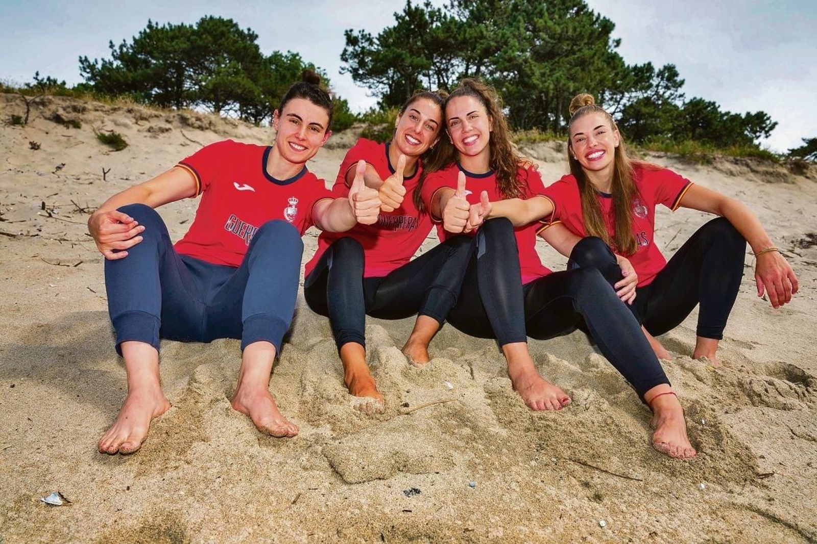 Paulina Buforn, Jennifer Gutiérrez, Carmen Campos y Paula Arcos dan el ‘ok’ sentadas en la arena de la playa de O Muíño, justo donde el río Miño se une con el oceáno Atlántico.