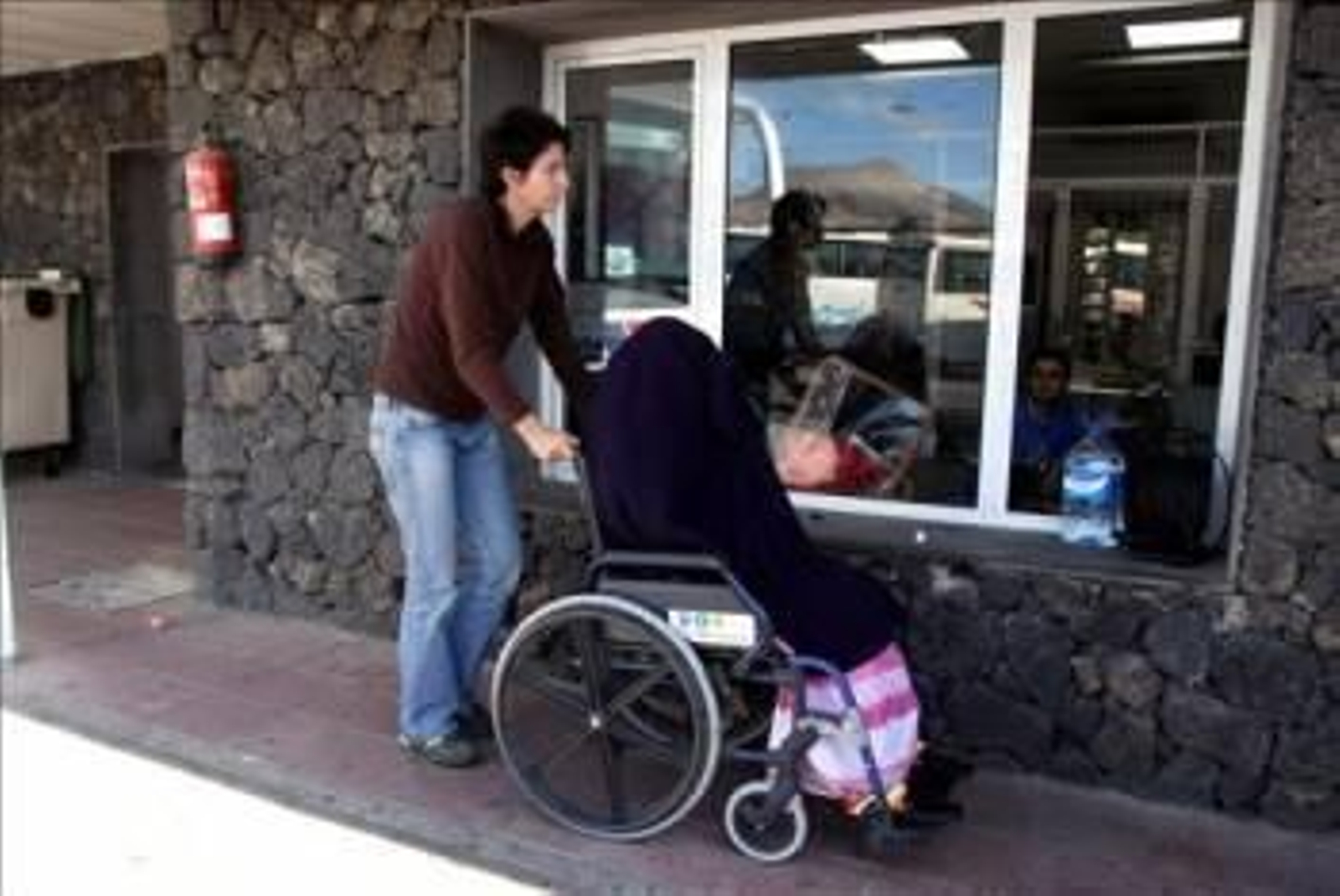 En la imagen, una mujer traslada a Haidar (en silla de ruedas) a una pequeña habitación, en la terminal de autobuses del aeropuerto de Lanzarote, para que descanse.