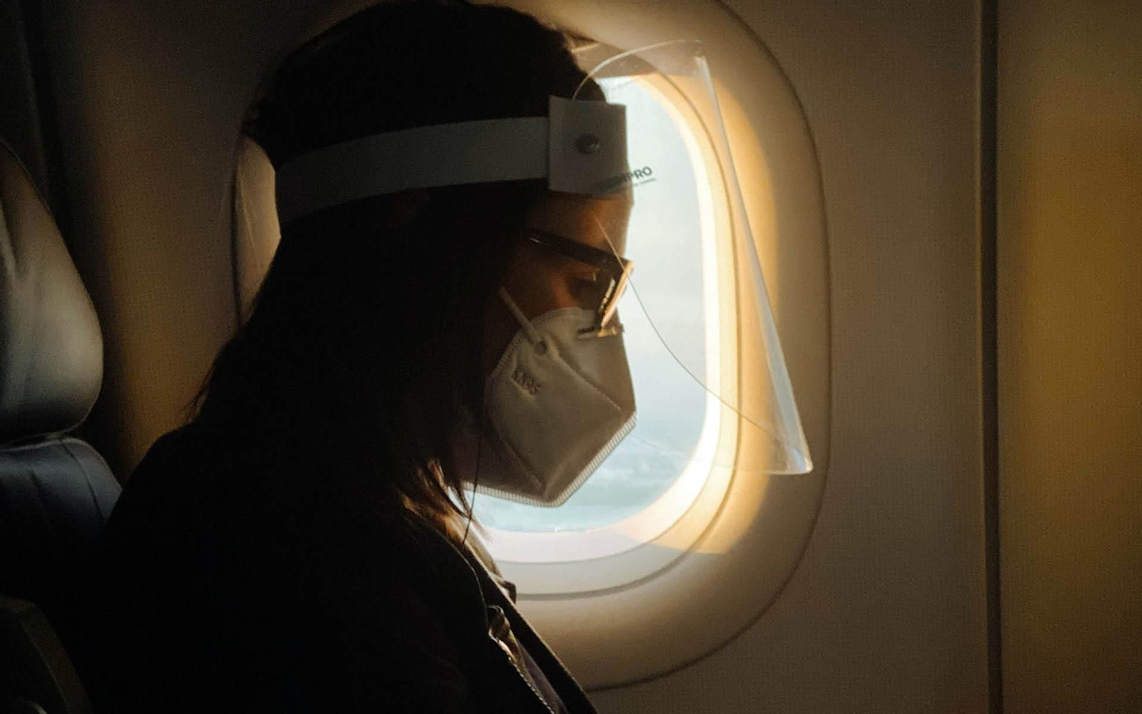 Una mujer viaja en un avión con mascarilla y pantalla protectora. (Foto: Unsplash)