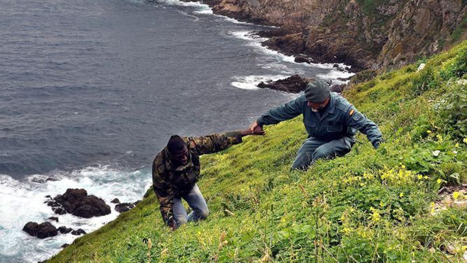 En la imagen un Guardia Civil ayuda a un inmigrante a subir un acantilado tras arribar a tierra
