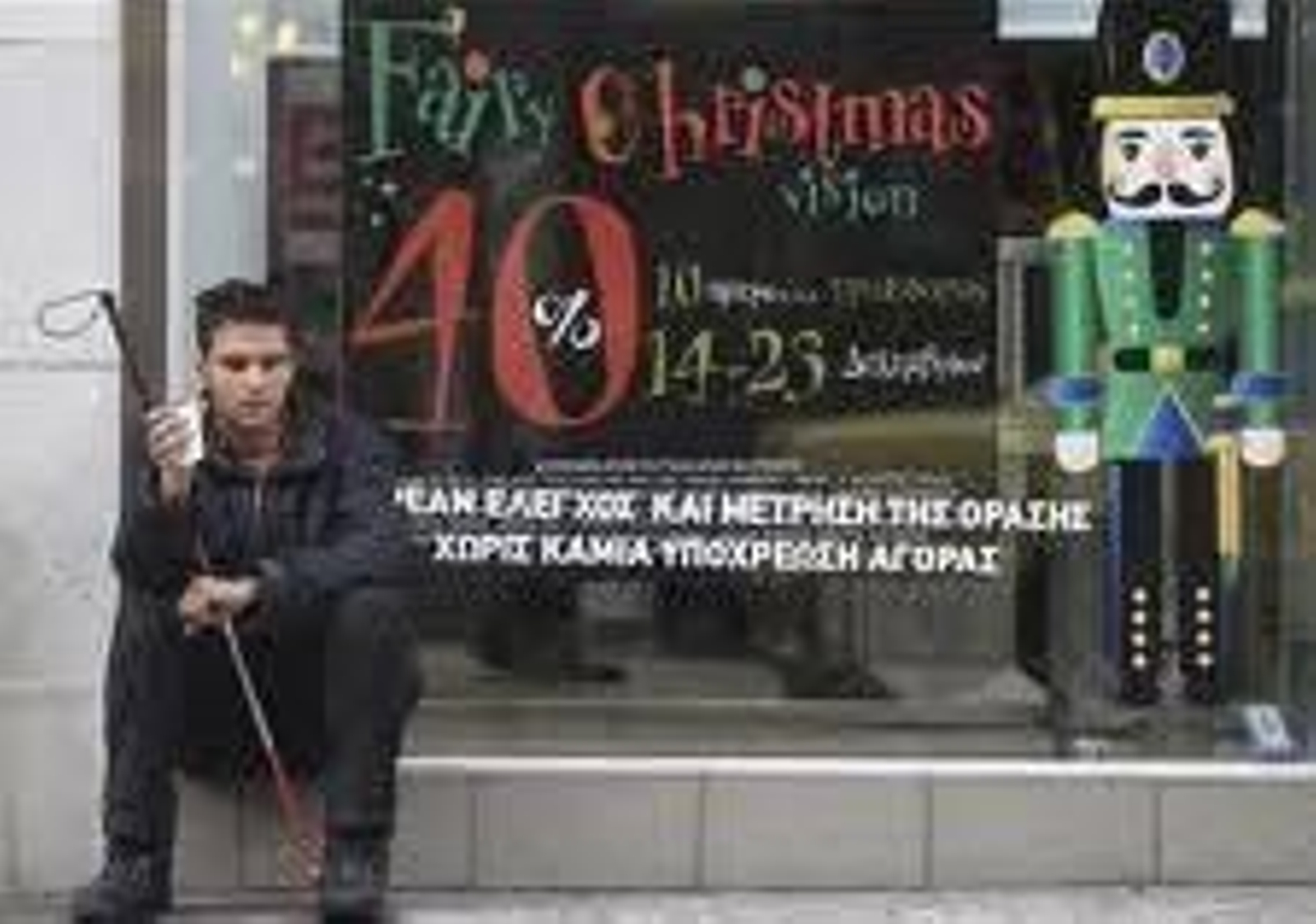 Un chico invidente espera el autobús sentado en el escaparate de una tienda.