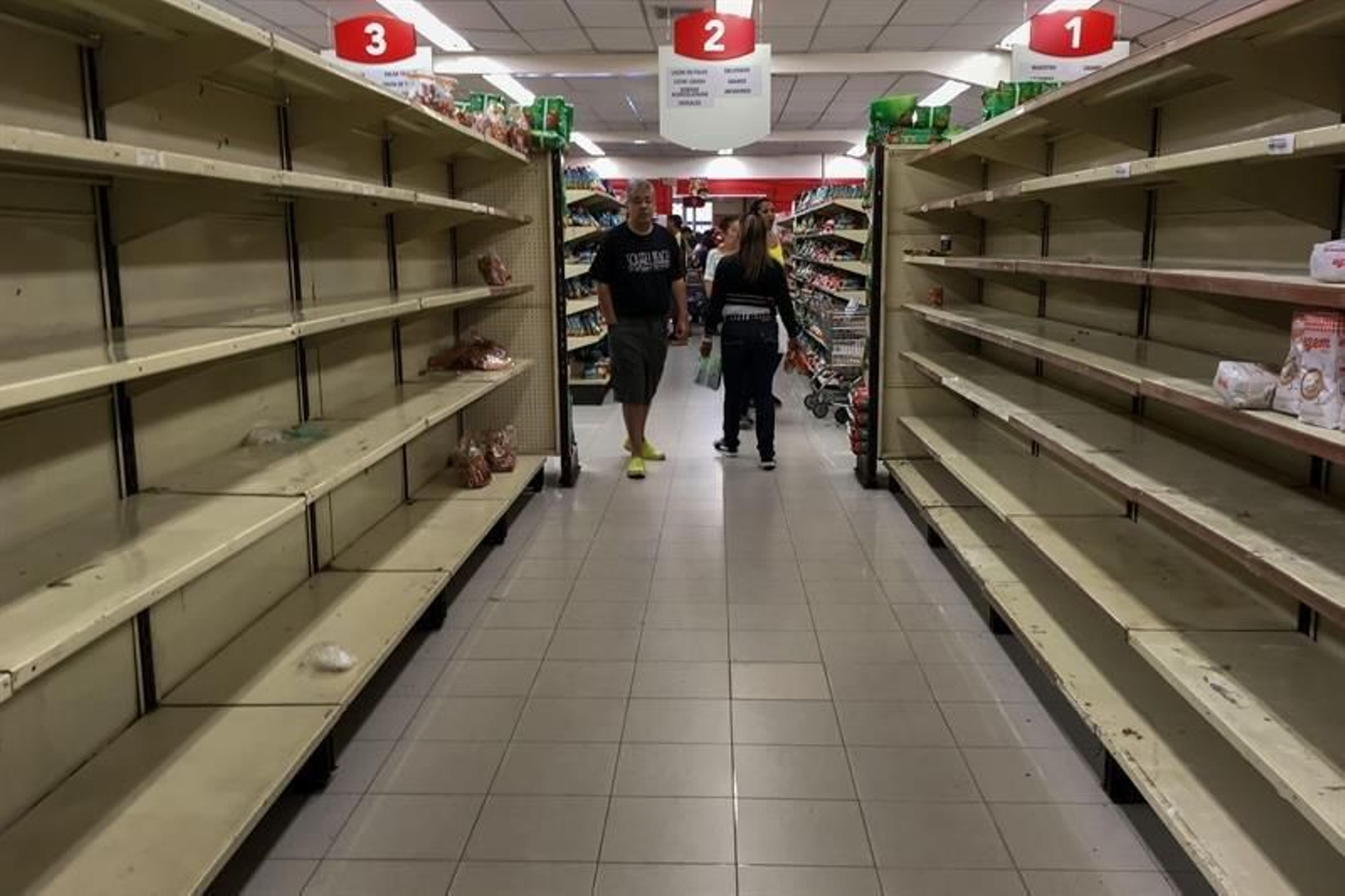 Personas buscando alimentos en un supermercado de Caracas, con muchas estanterías vacías.