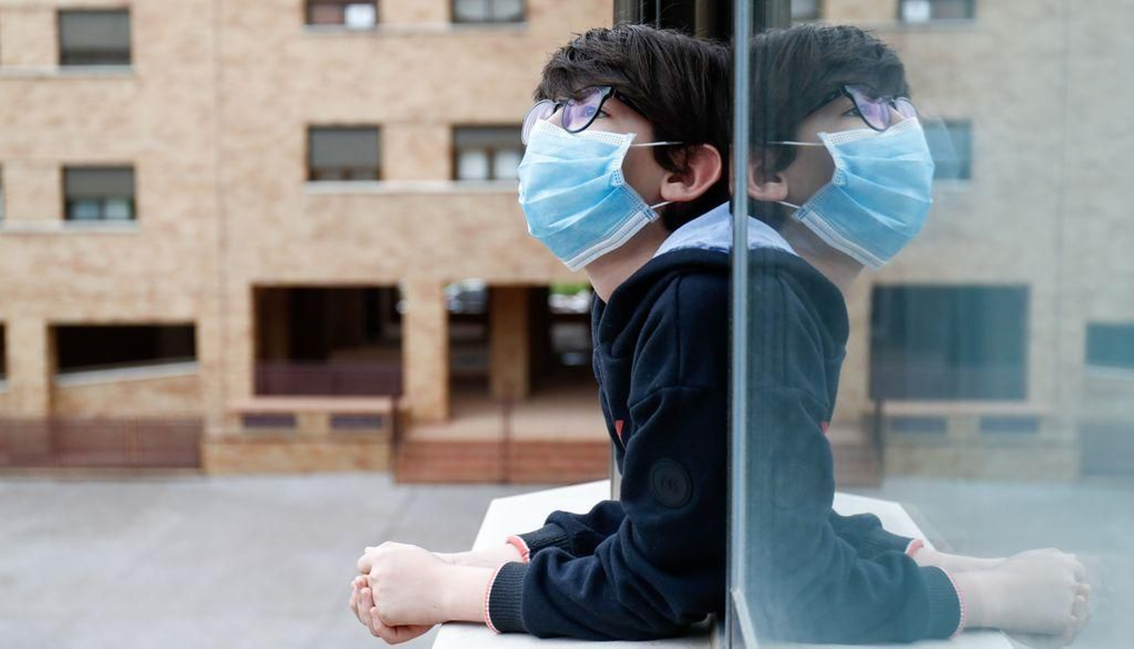 Un niño con mascarilla en la ventana de su casa.