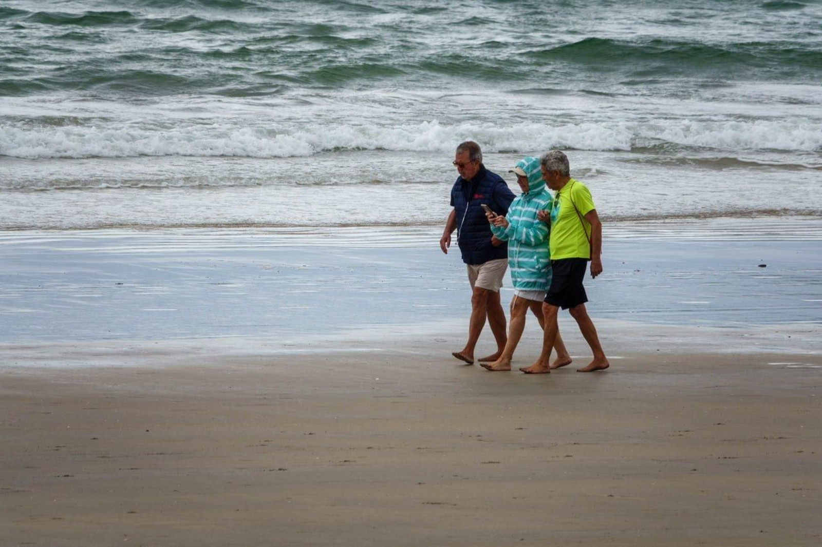 Tres personas caminan por la playa de Sanil. // Vicente Alonso