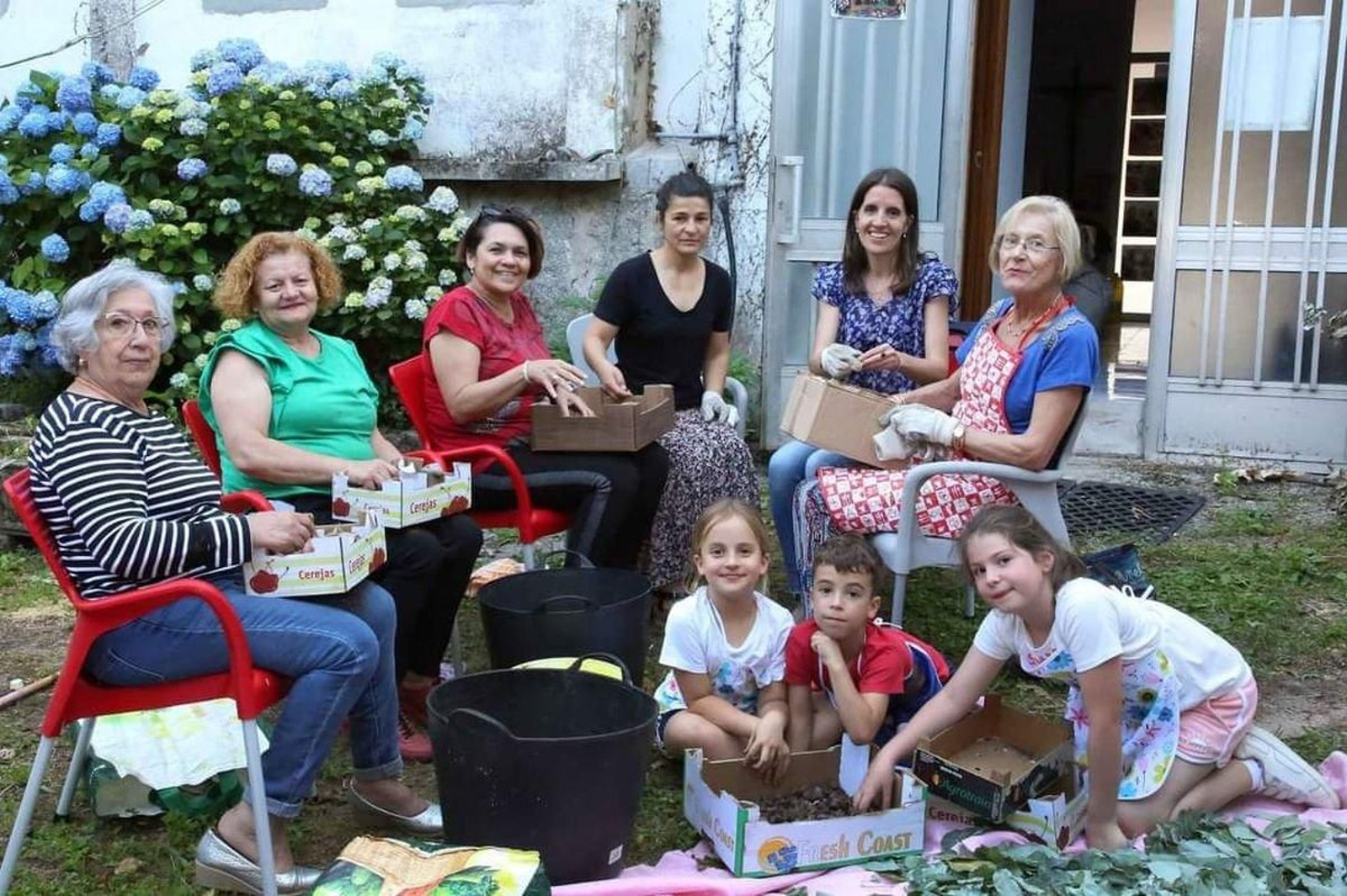 Vecinas de todas las edades, deshojando material en un portal de Corpus al aire libre.