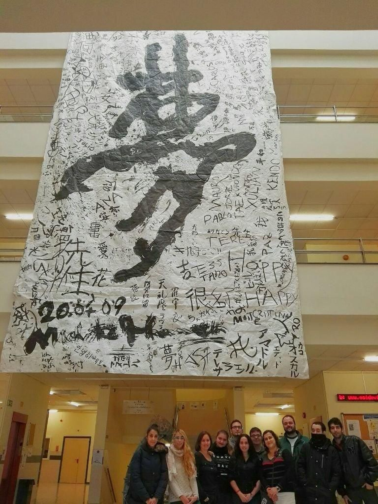 Alumnos de japonés posan bajo el cartel escrito con caligrafía del país nipón.