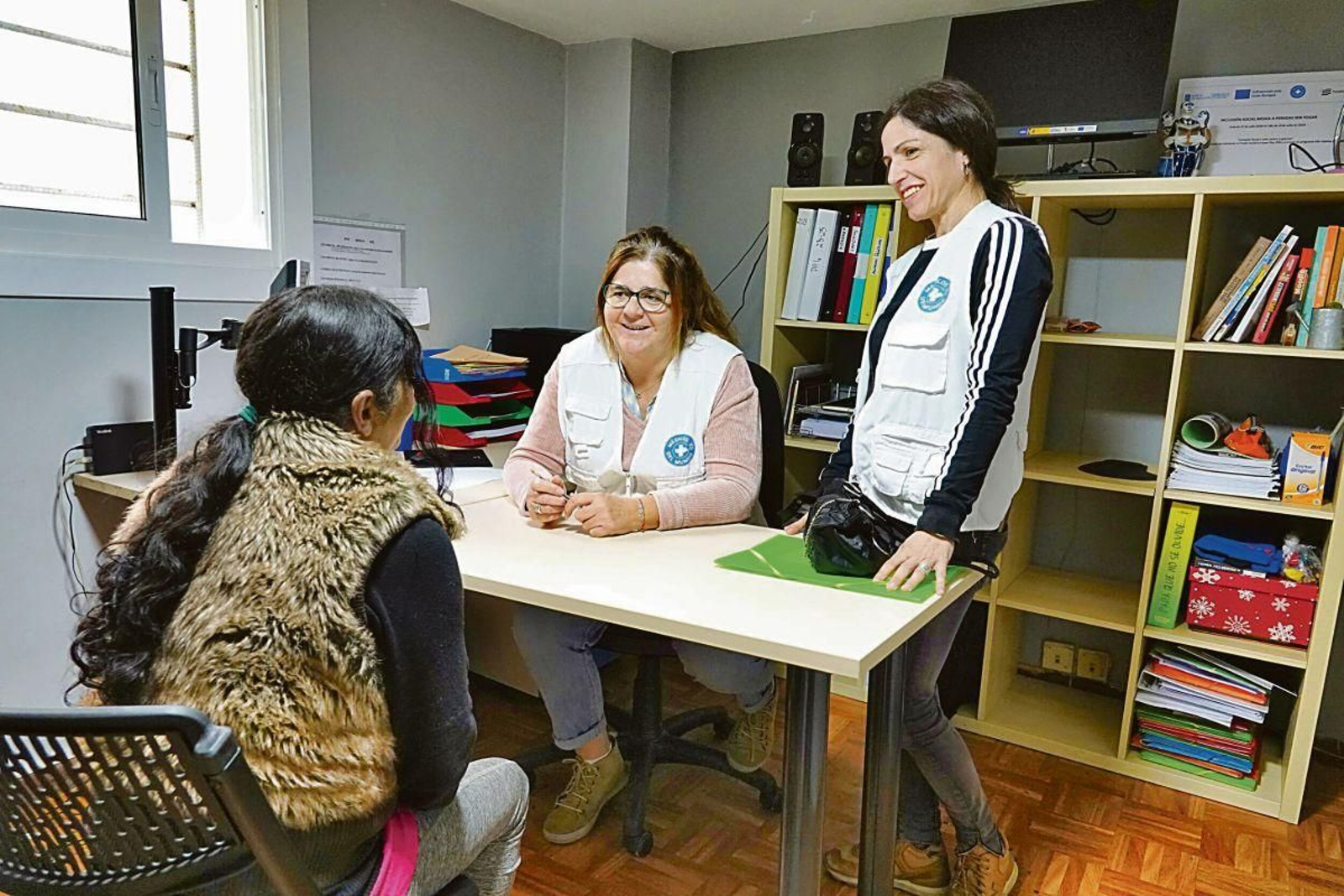 La coordinadora, de pie, y la trabajadora social con una usuaria.