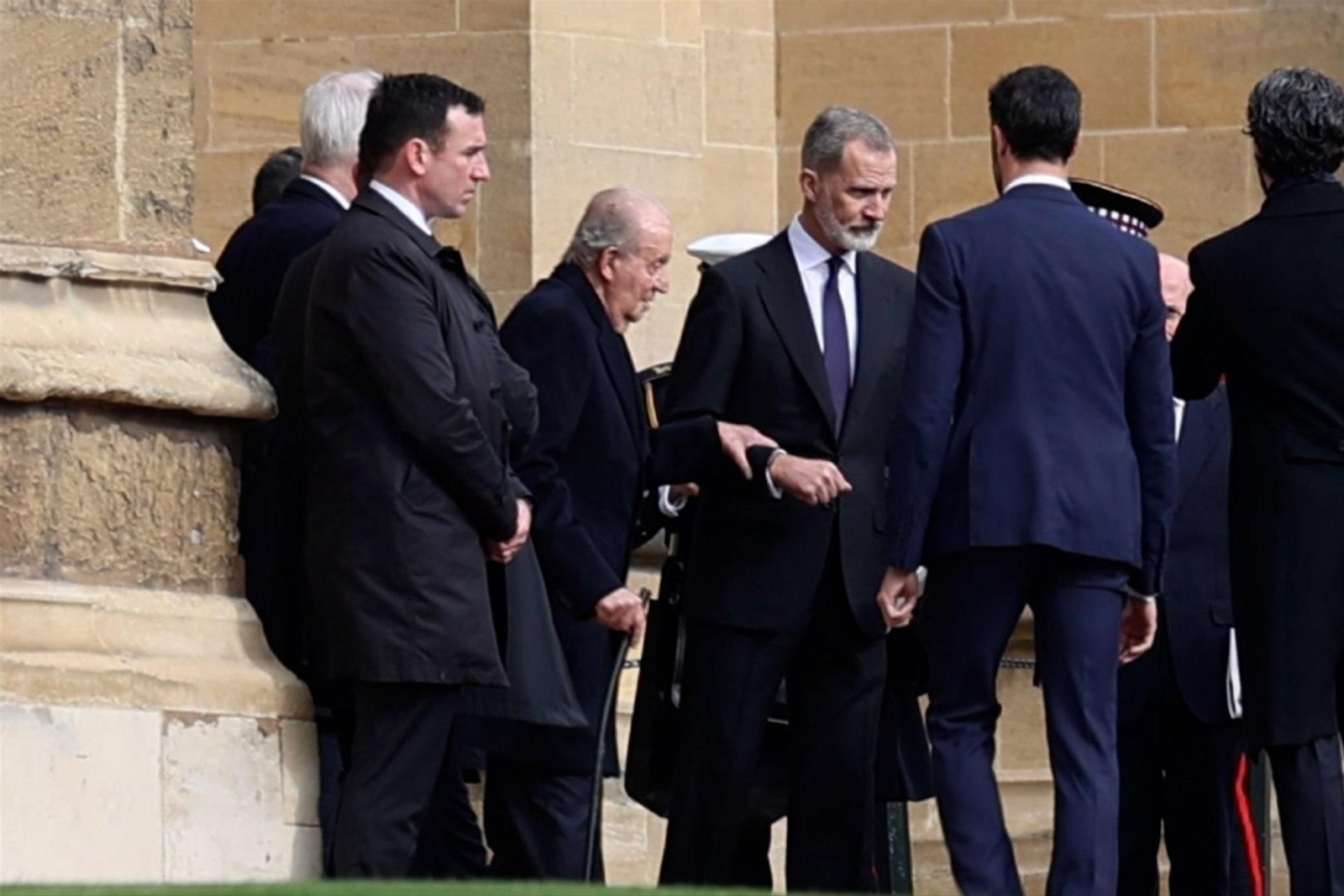 El rey emérito Juan Carlos I, agarrado del brazo de su hijo, Felipe VI, tras la misa por el rey Constantino de Grecia, en Windsor. // EP