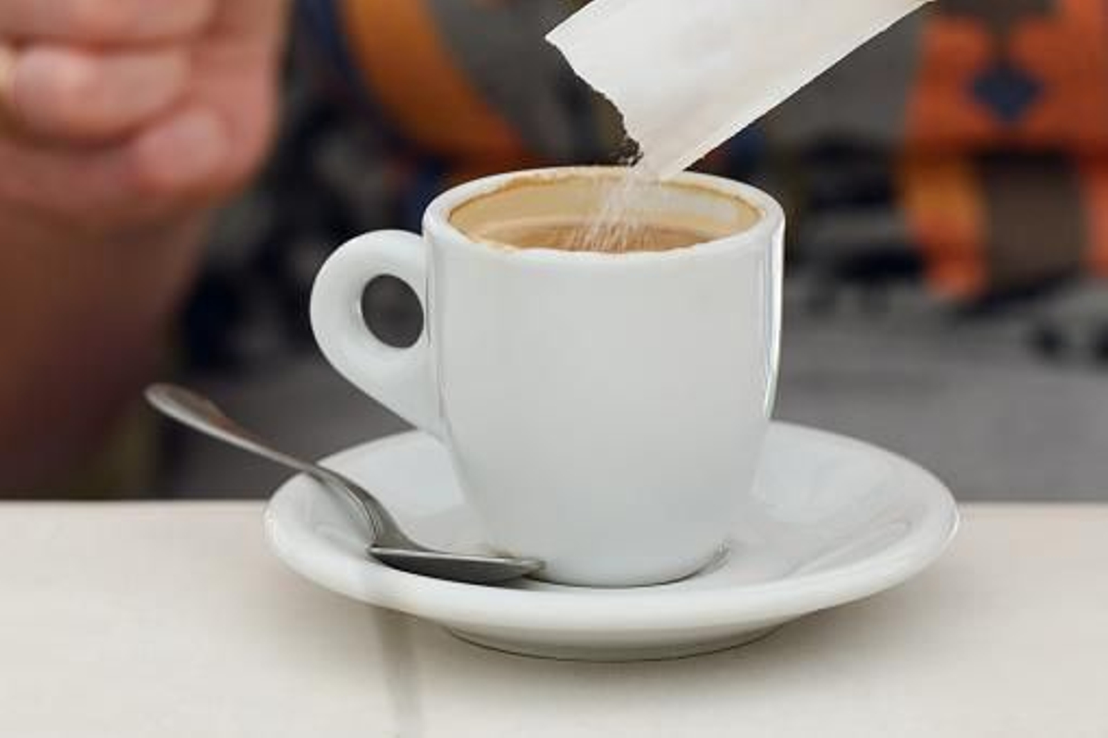 Una persona vierte un sobre de azúcar en una taza de café.