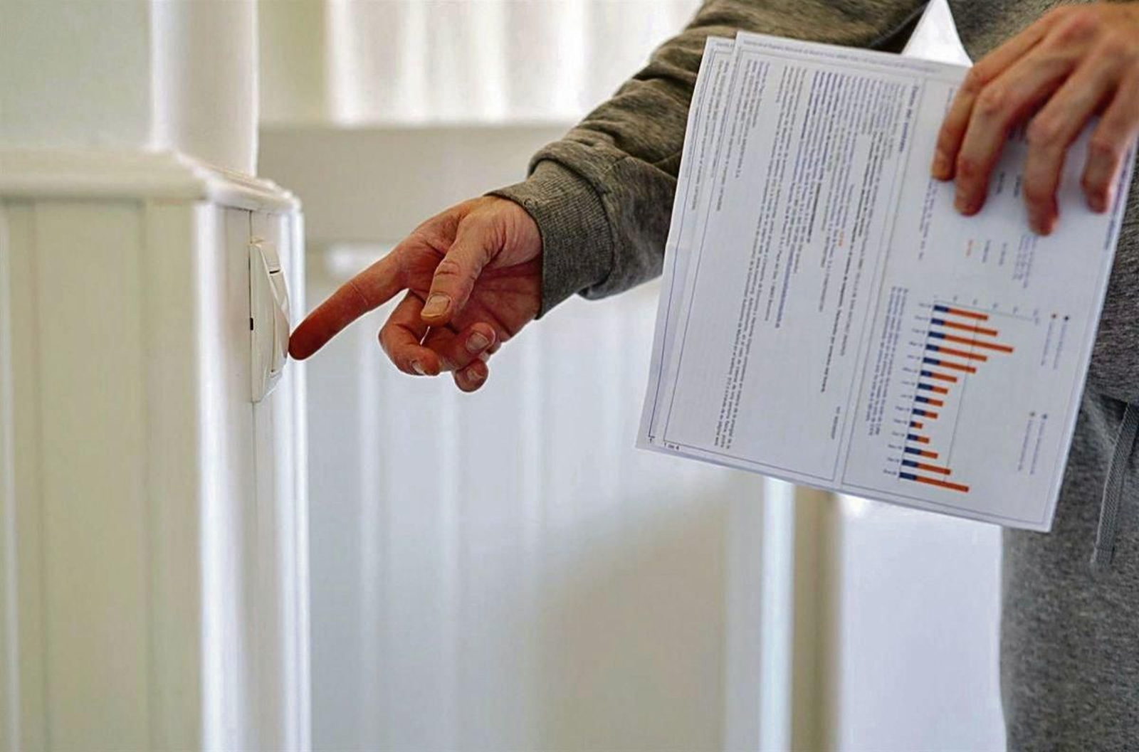 Un hombre enciende un interruptor con una factura de luz en la mano