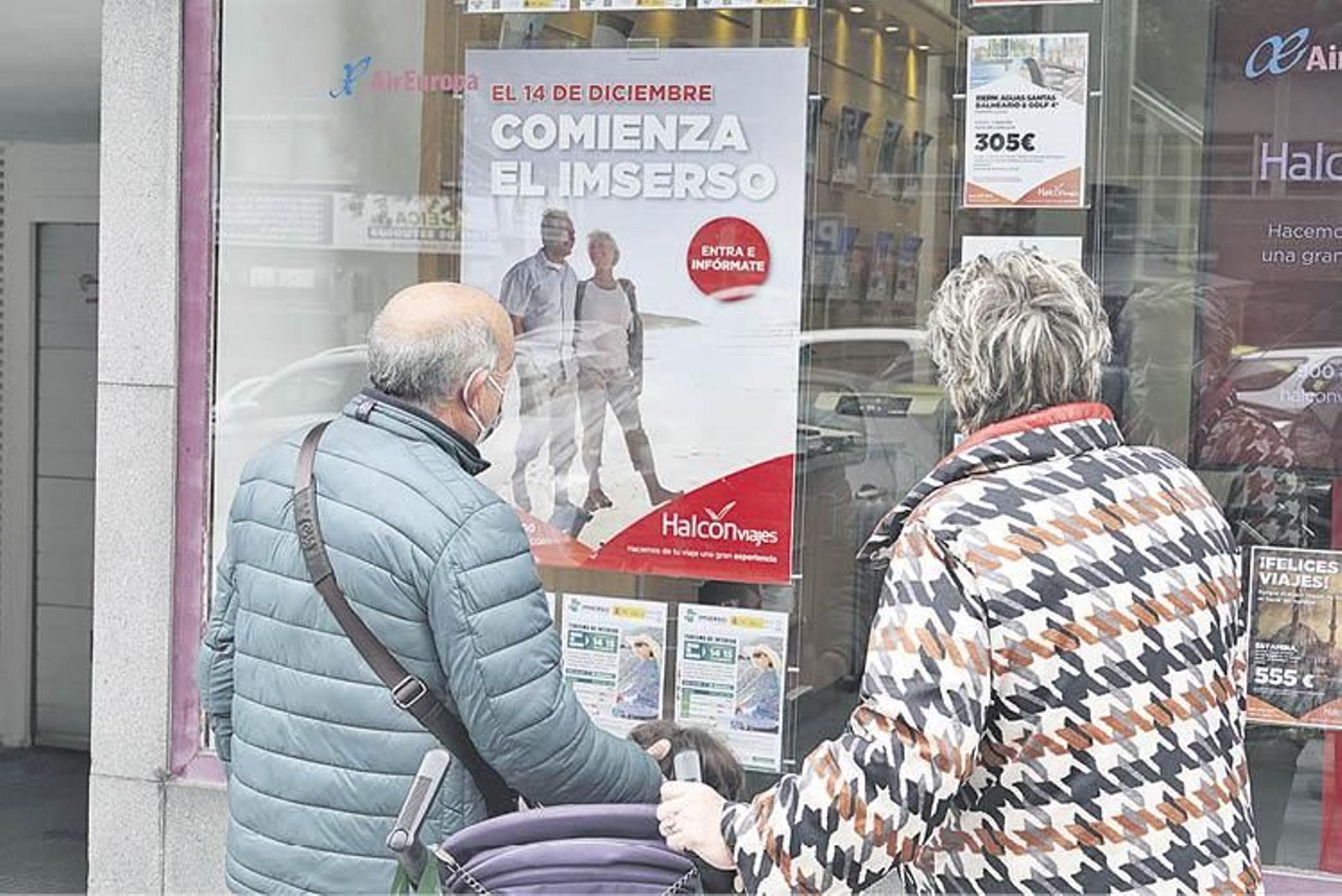 Dos personas ante el escaparate de una agencia de viajes que anuncia el Imserso.