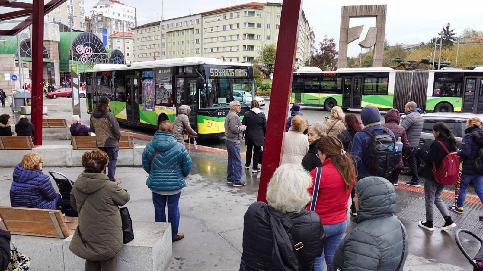 Varias personas esperan en una parada la llegada de su autobús.