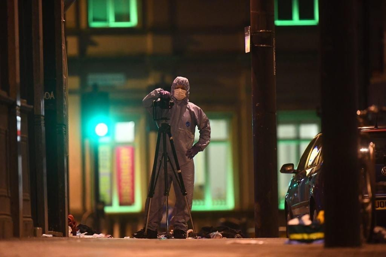 Un miembro del equipo forense trabaja en el lugar de los hechos, con objetos ensangrentados en el suelo.