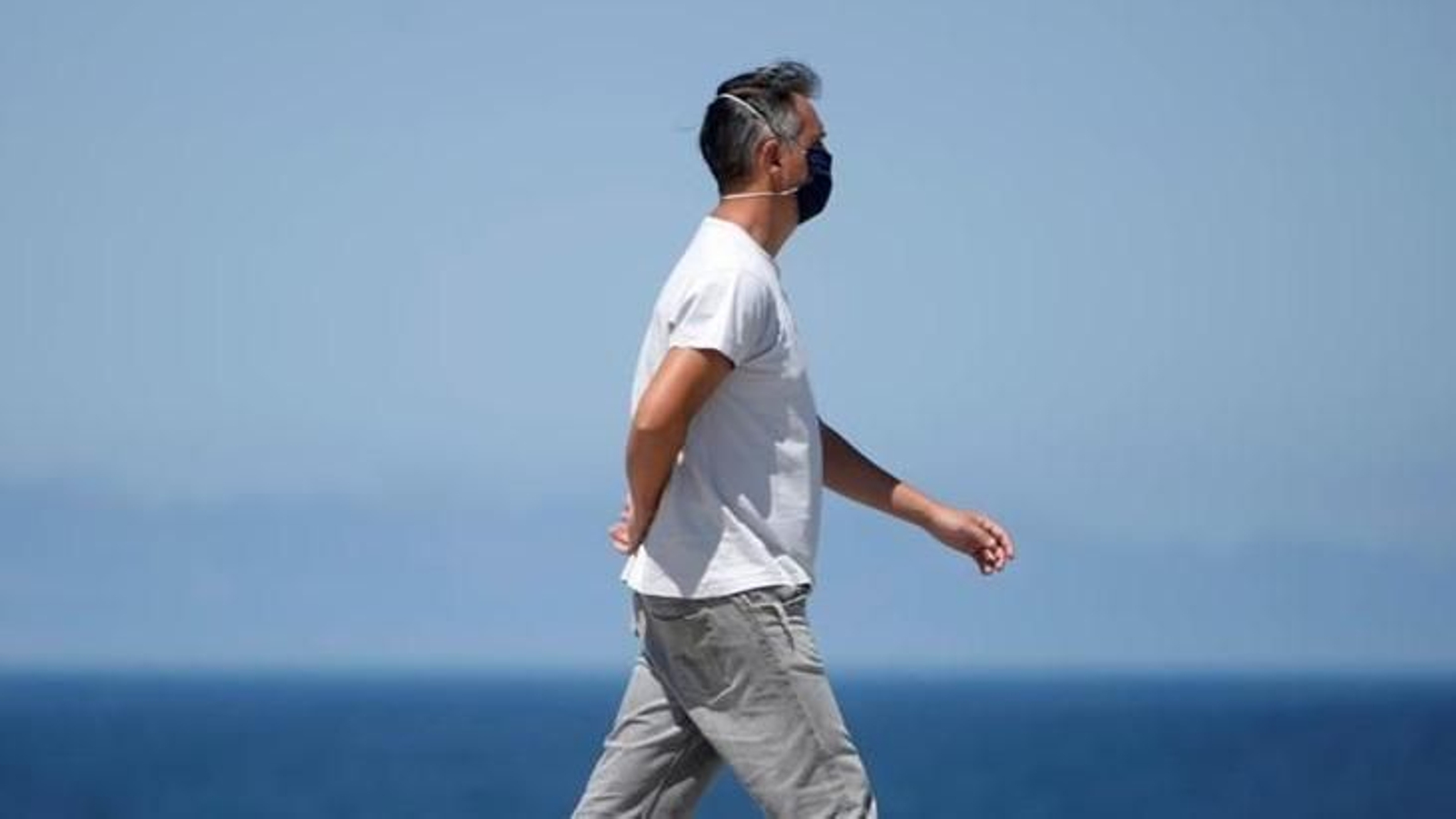 Un hombre camina, solitario y protegido, por el paseo marítimo de A Coruña.