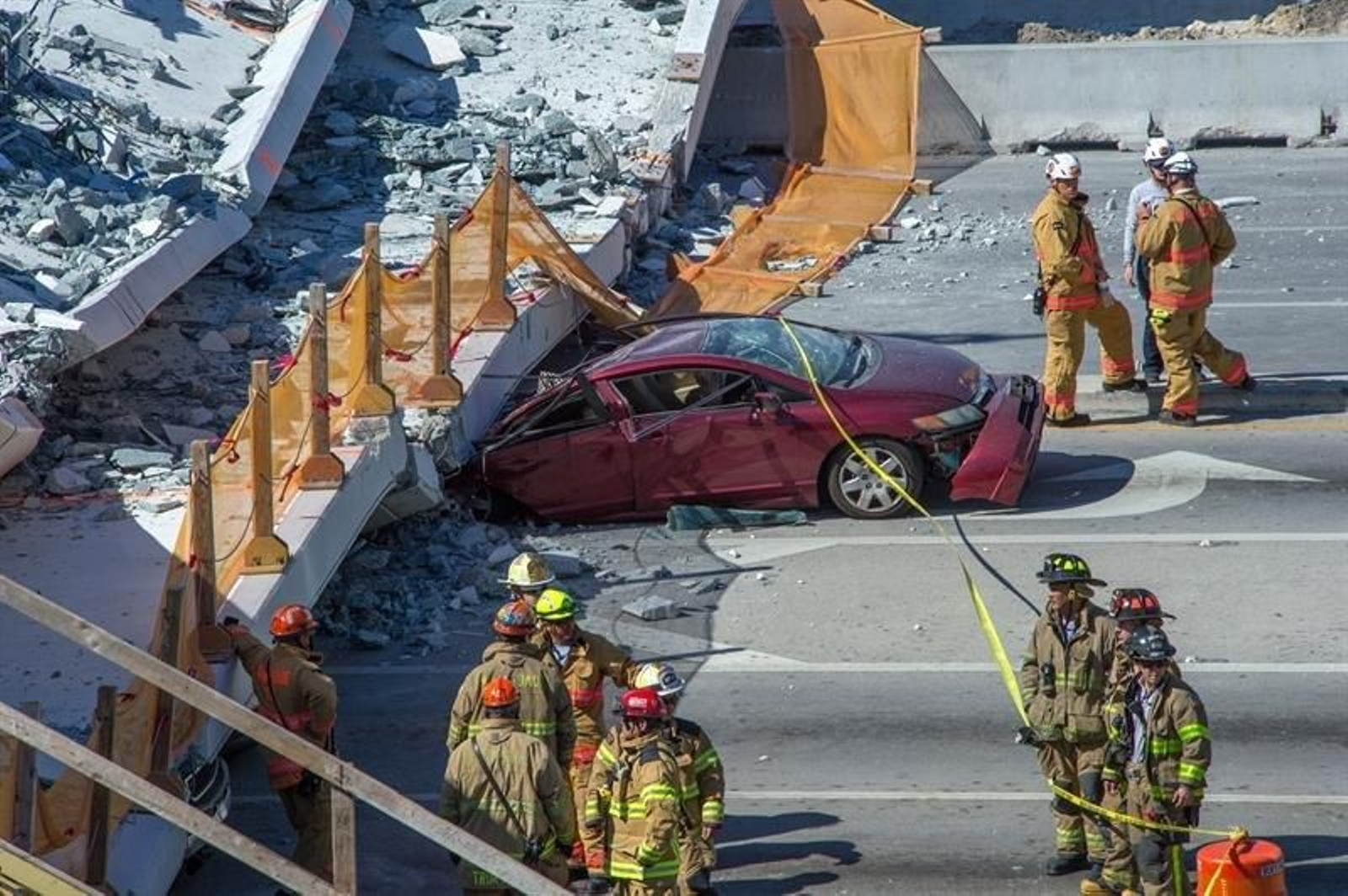 Varios miembros del departamento de bomberos trabajan en el puente para peatones que se ha derrumbado hoy