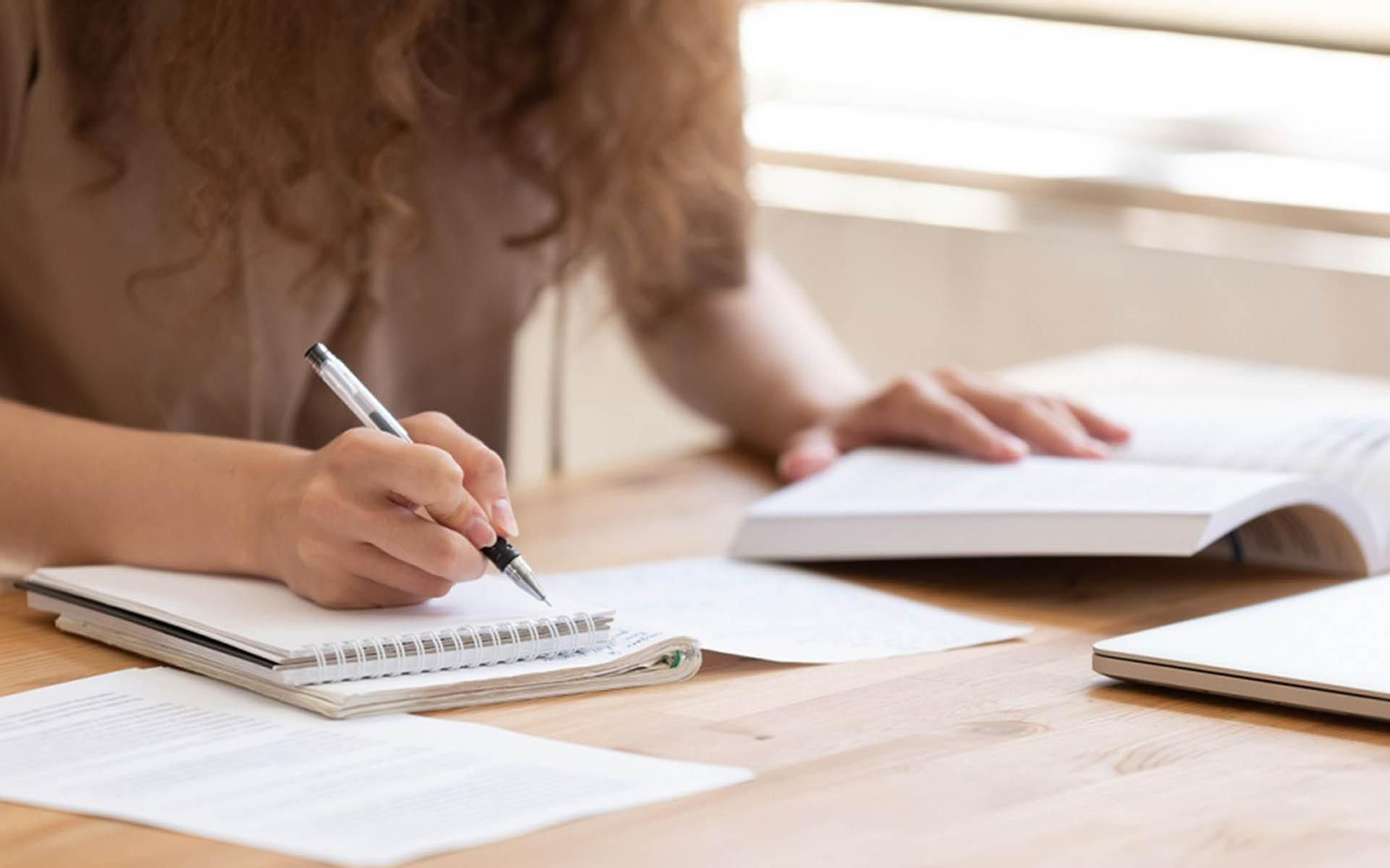 Close up of female student sit at table study using  handbook write in notebook doing research, motivated girl prepare for test or exam learning handwriting in workbook, making notes of important data