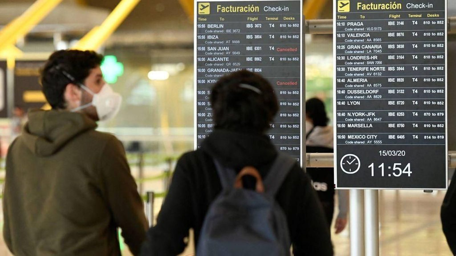 Dos pasajeros protegidos con mascarillas consultan los vuelos en el aeropuerto de Barajas.