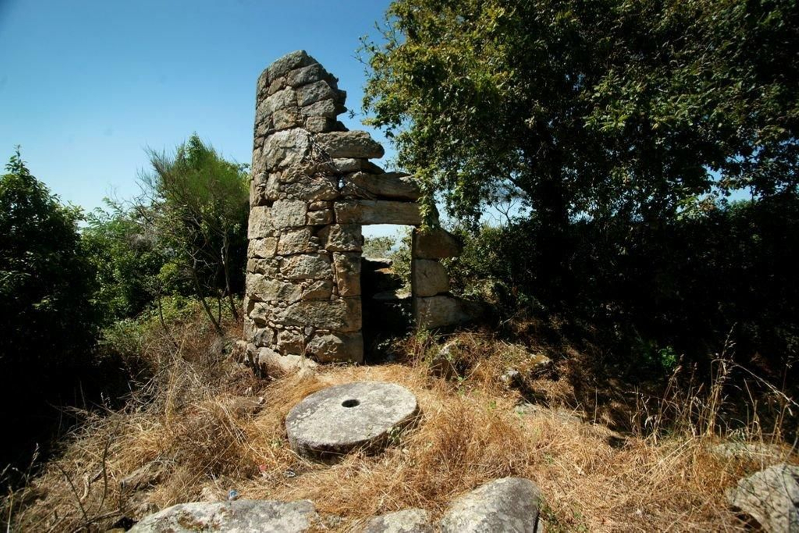 La puerta y parte del muro del molino se mantene en pie, en primer plano se encuentra la piedra de moler.