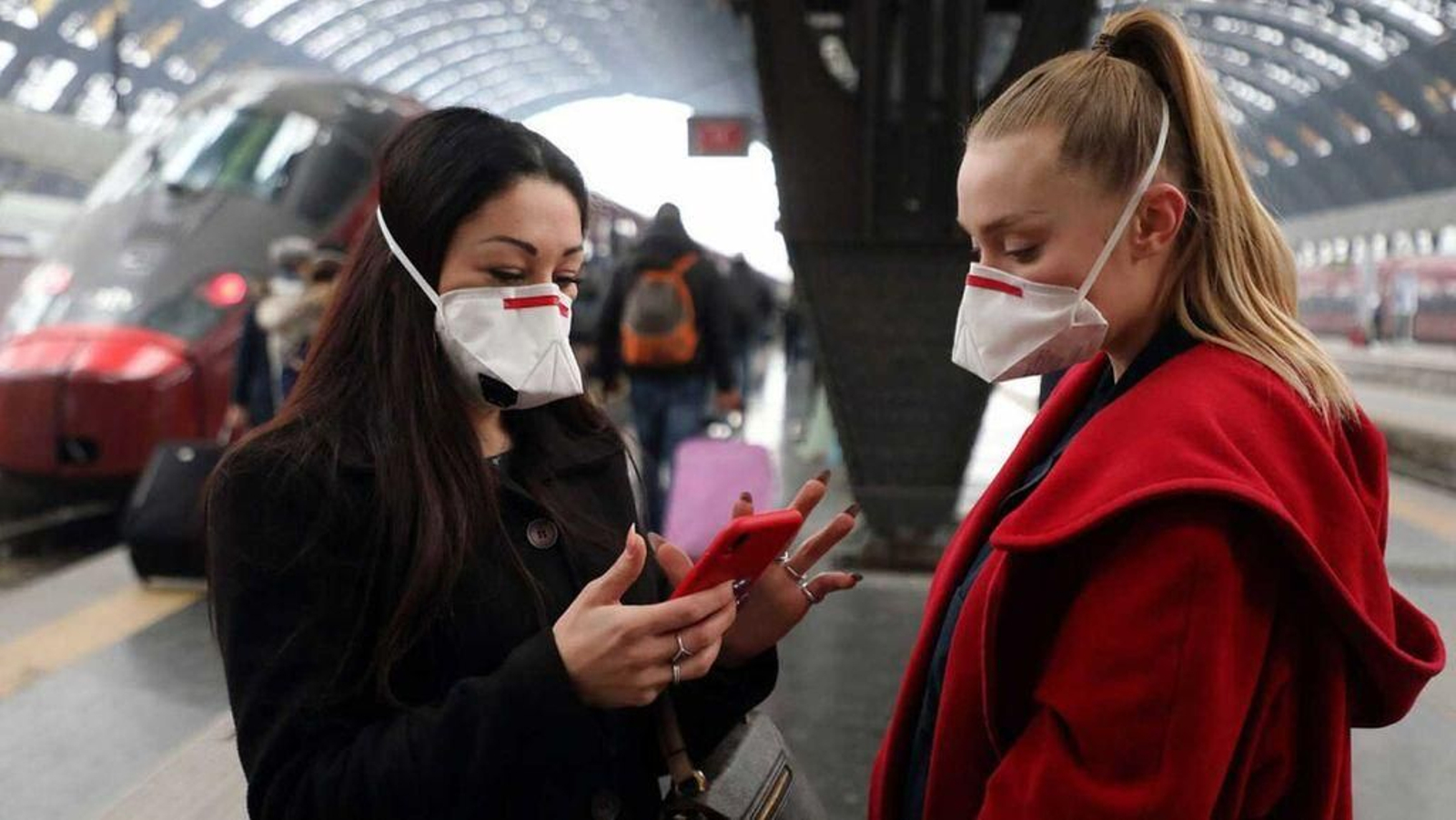 Dos jóvenes estudiantes, protegidas con mascarilla, en la estación de tren de Milán (Italia)